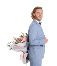 Young handsome man in stylish suit hiding beautiful flower bouquet behind his back on white background