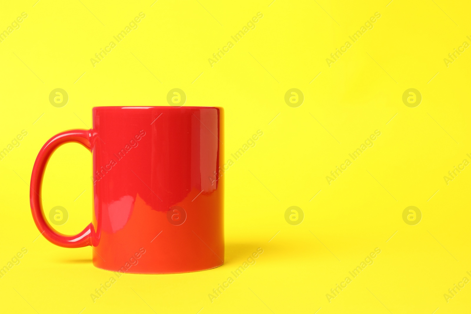Photo of One red ceramic mug on yellow background, space for text