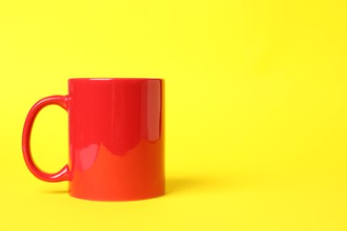 Photo of One red ceramic mug on yellow background, space for text