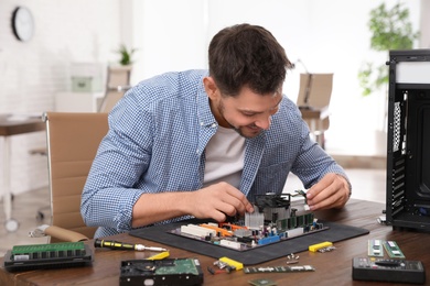 Photo of Male technician repairing motherboard at table indoors