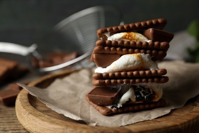 Delicious marshmallow sandwiches with crackers and chocolate on wooden table, closeup