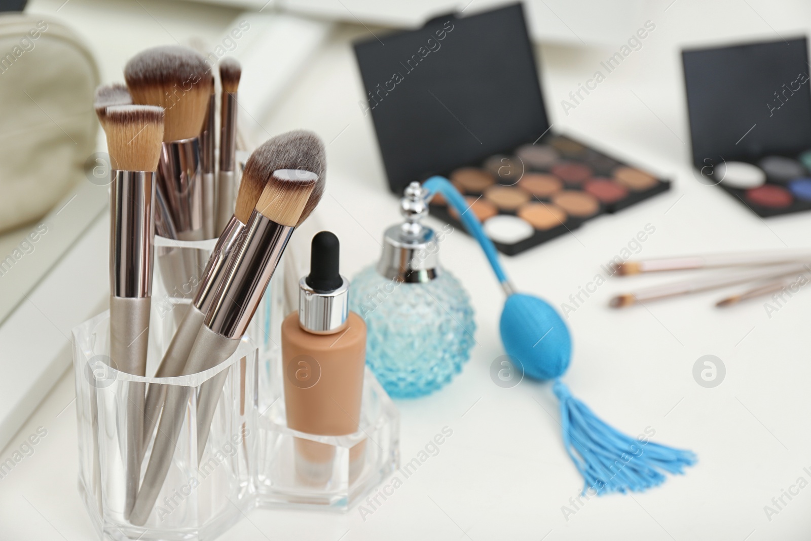 Photo of Different makeup products and bottle of perfume on white dressing table