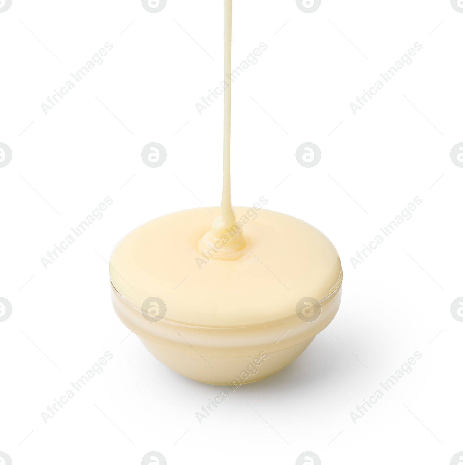 Photo of Pouring condensed milk into glass bowl isolated on white