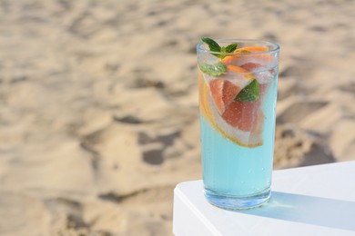 Photo of Glass of refreshing drink with grapefruit and mint on white table at beach, space for text