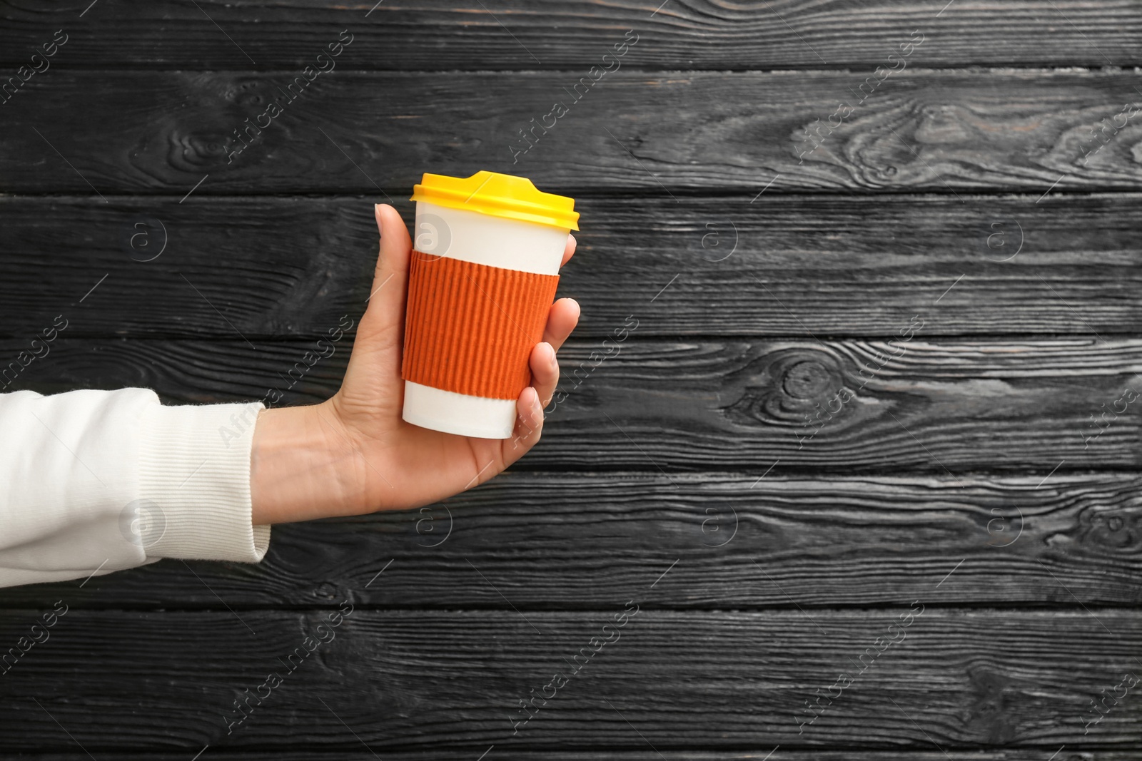 Photo of Woman holding takeaway paper coffee cup on wooden background. Space for text
