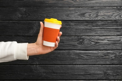 Woman holding takeaway paper coffee cup on wooden background. Space for text