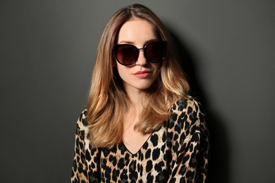 Photo of Young woman wearing stylish sunglasses on dark grey background