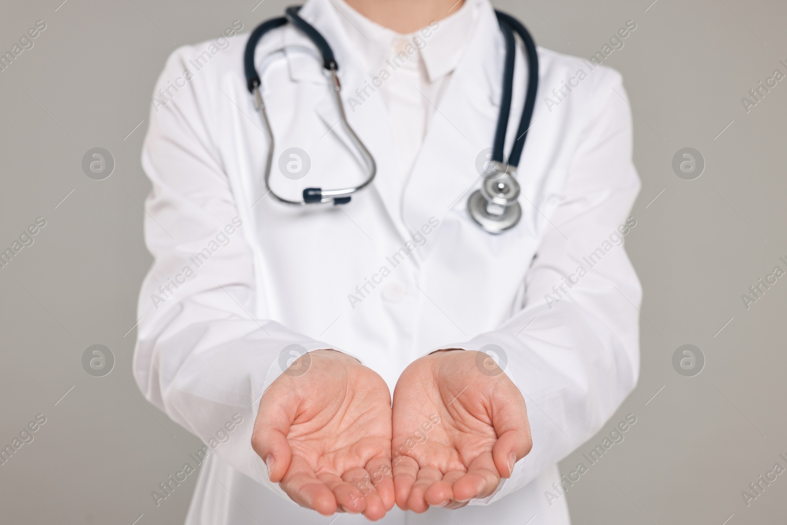 Photo of Doctor with stethoscope holding something on grey background, closeup