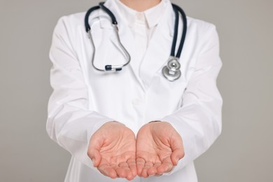 Doctor with stethoscope holding something on grey background, closeup