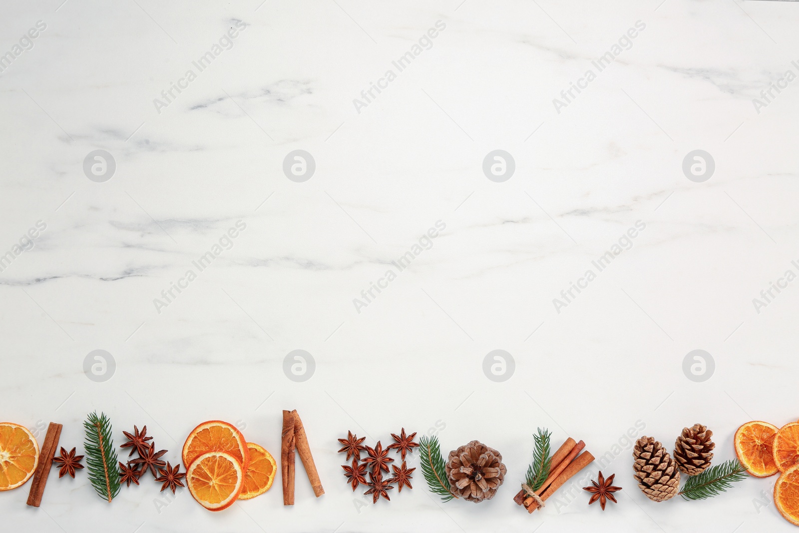 Photo of Dry orange slices, cinnamon sticks, fir branches and anise stars on white marble table, flat lay with space for text