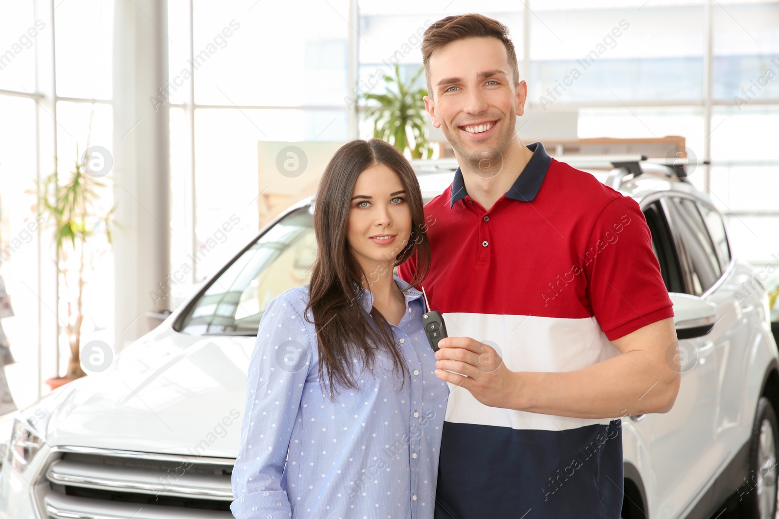 Photo of Young couple with key in salon. Buying new car