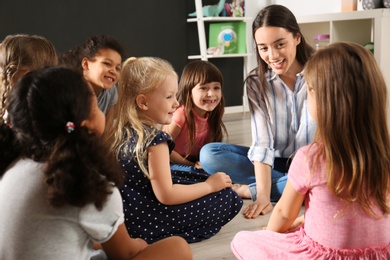 Photo of Cute little children with nursery teacher in kindergarten. Indoor activity