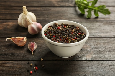 Photo of Bowl with mix of peppercorns and garlic on wooden table