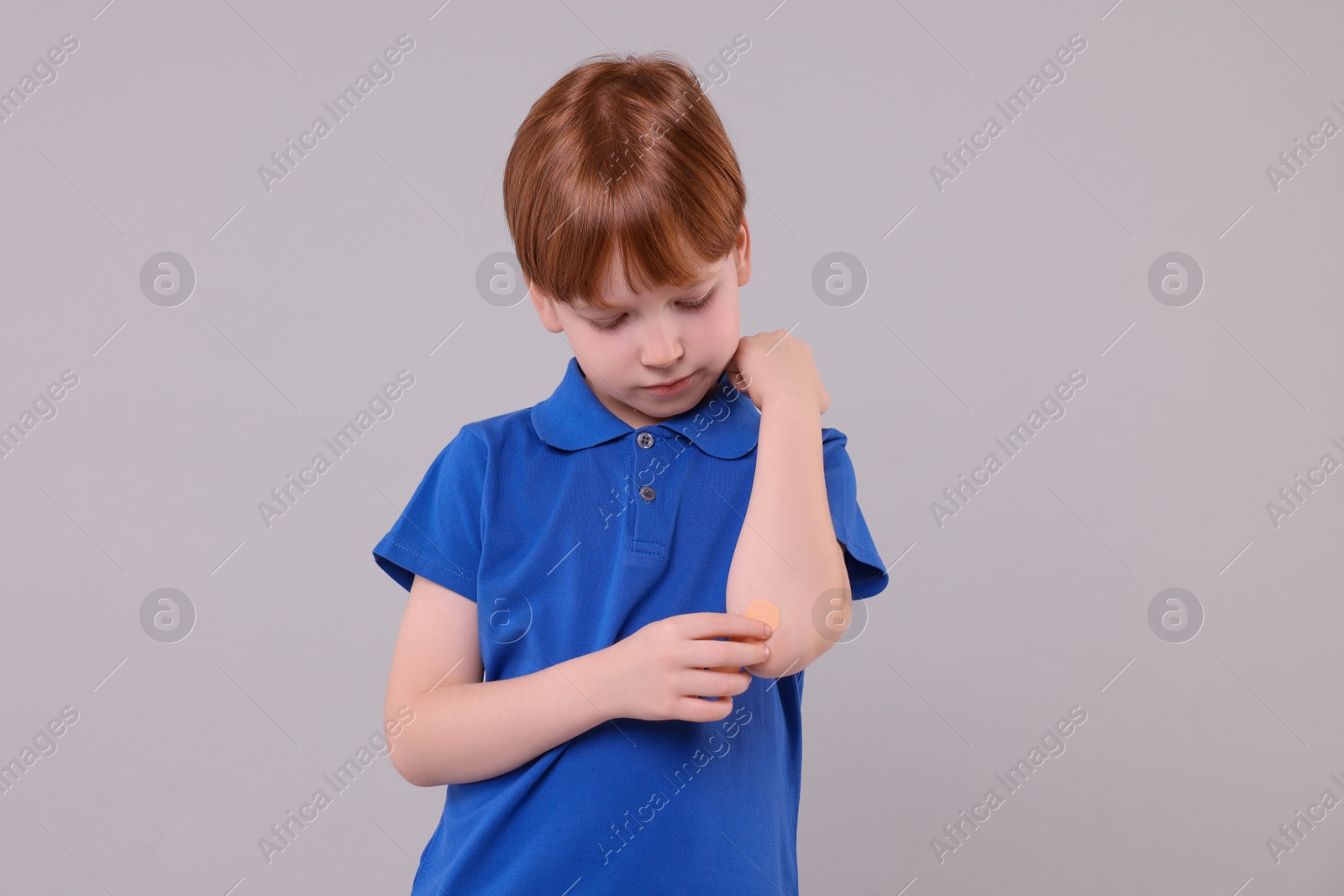 Photo of Little boy putting sticking plaster onto elbow against light grey background