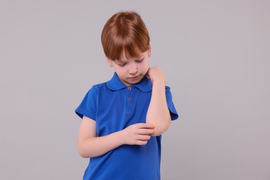 Little boy putting sticking plaster onto elbow against light grey background