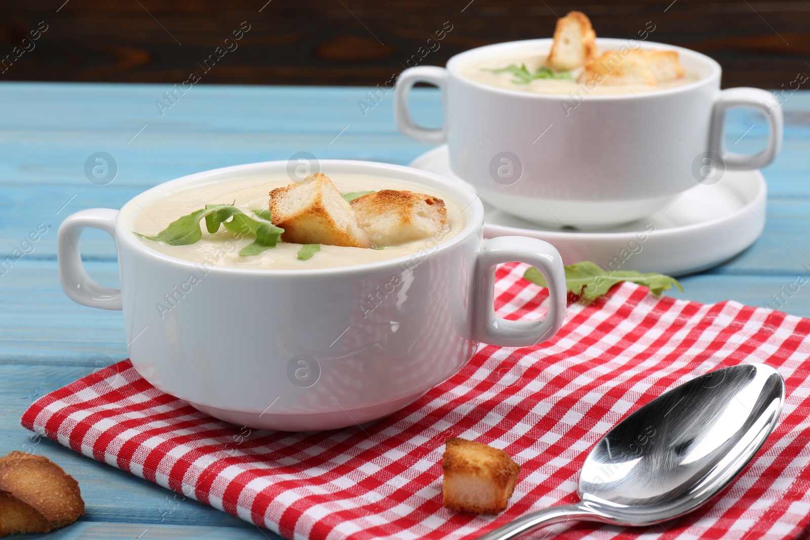 Photo of Bowls with tasty creamy soup of parsnip served on light blue wooden table, closeup