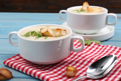 Photo of Bowls with tasty creamy soup of parsnip served on light blue wooden table, closeup