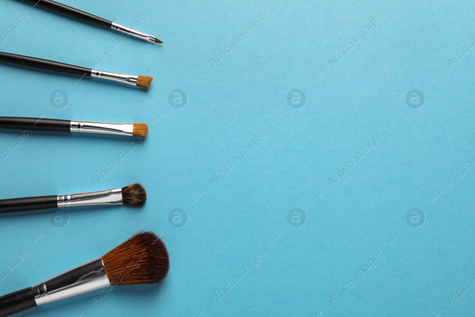 Photo of Set of makeup brushes on light blue background, flat lay. Space for text