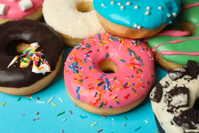 Photo of Different delicious glazed doughnuts on light blue background, closeup