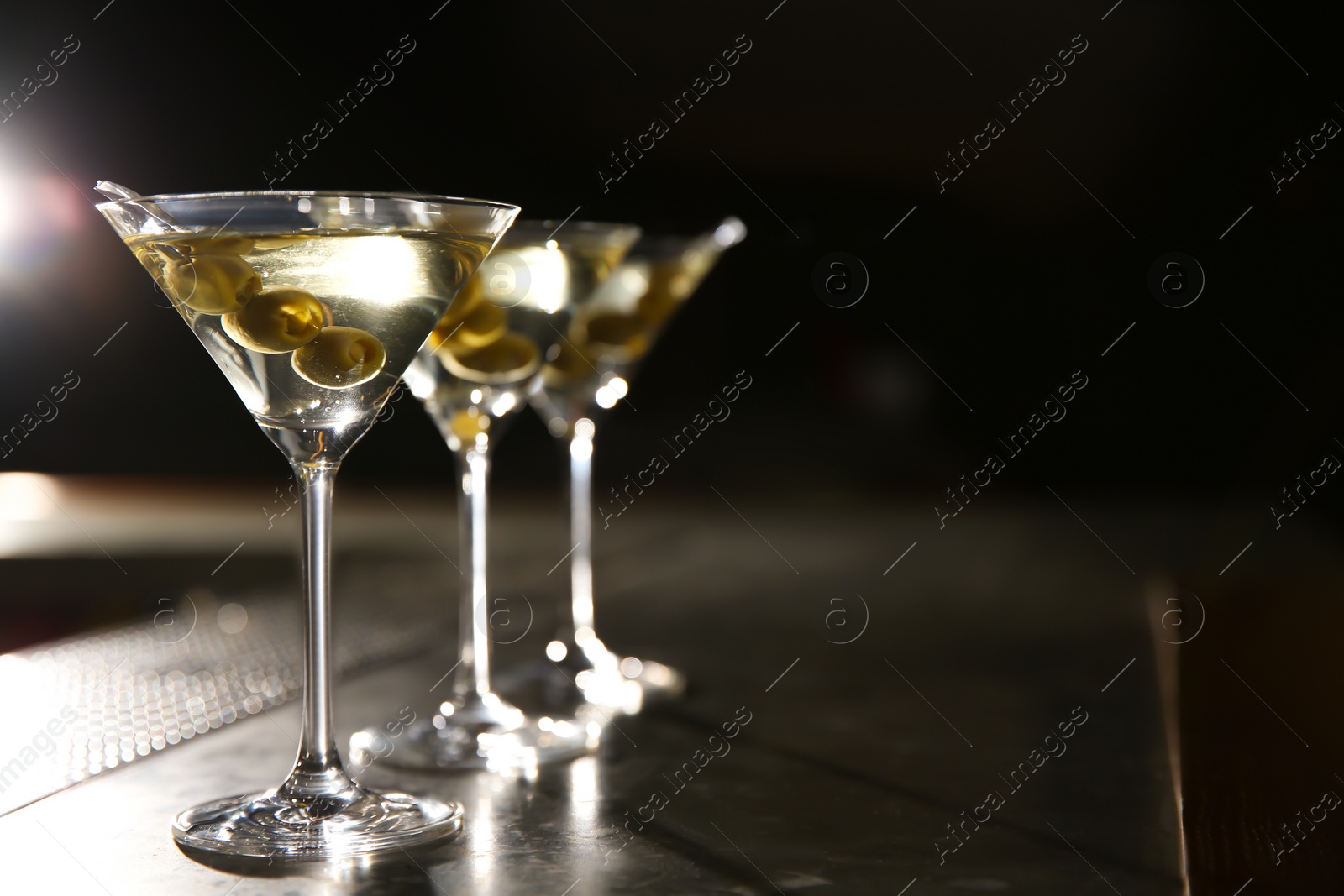 Photo of Glasses of martini cocktail with olives on bar counter. Space for text