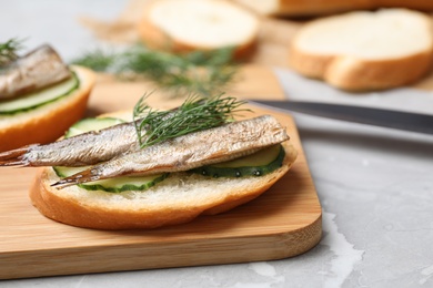 Photo of Delicious sandwich with sprats, cucumbers and dill on wooden board, closeup