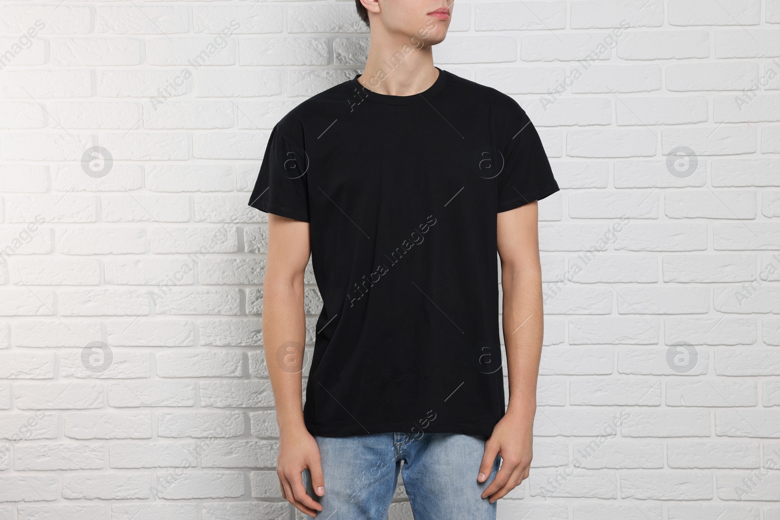 Photo of Man wearing black t-shirt near white brick wall, closeup. Mockup for design