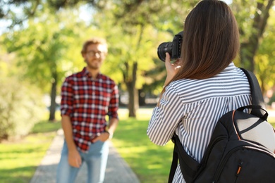 Photo of Young female photographer taking photo of man with professional camera in park