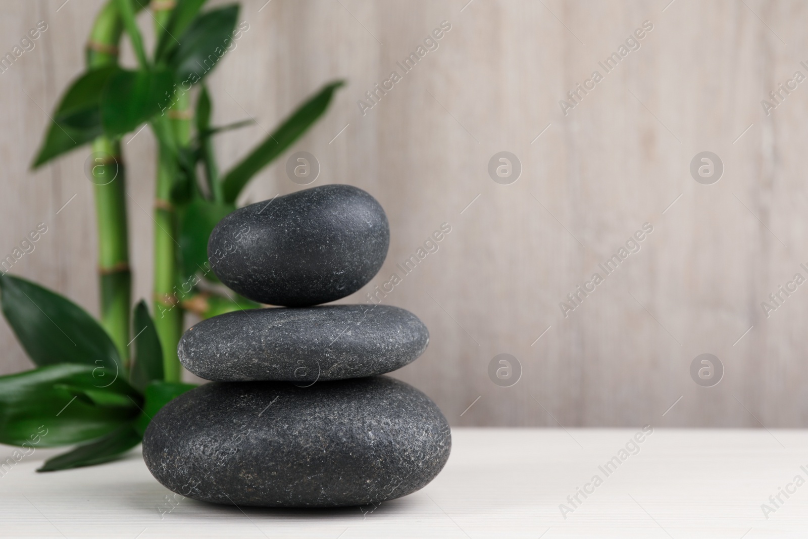 Photo of Stacked spa stones and bamboo on white wooden table. Space for text