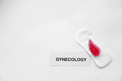 Photo of Flat lay composition with menstrual pad and red feather on light background. Gynecological care