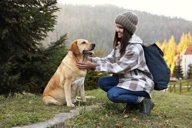 Happy woman and adorable dog sitting on green grass in mountains. Traveling with pet