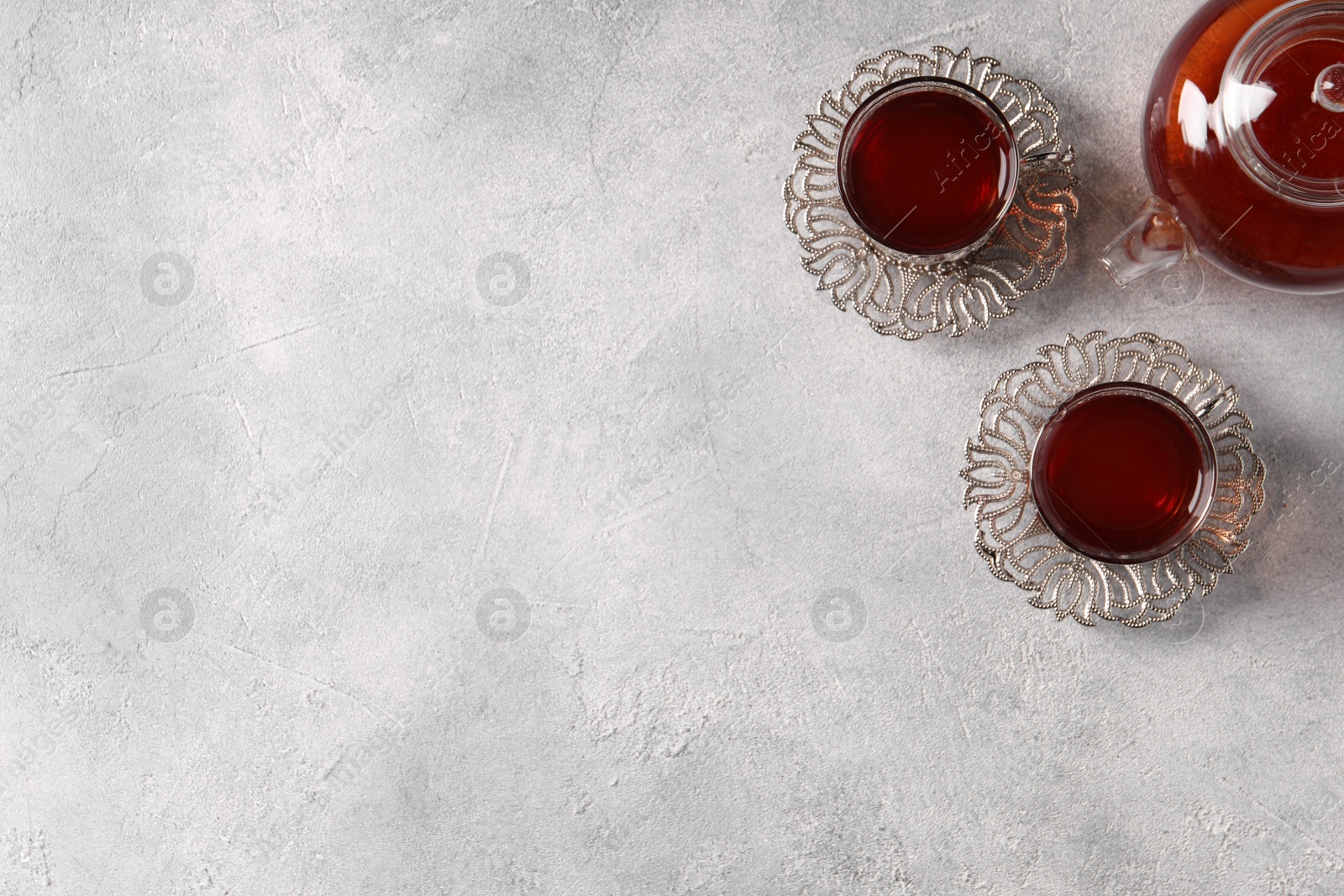 Photo of Glasses of traditional Turkish tea in vintage holders and pot on light grey table, flat lay. Space for text