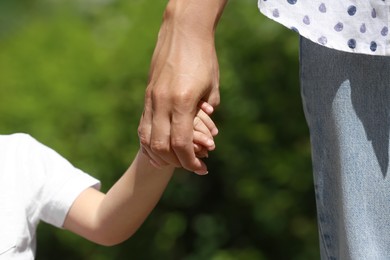 Photo of Mom and her child holding hands on blurred background, closeup