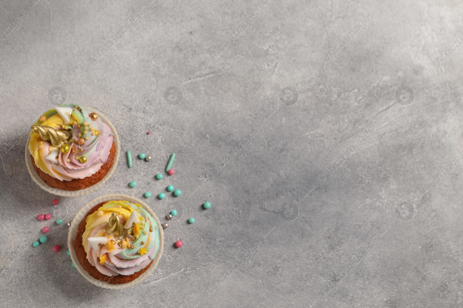 Photo of Cute sweet unicorn cupcakes on light grey table, flat lay. Space for text