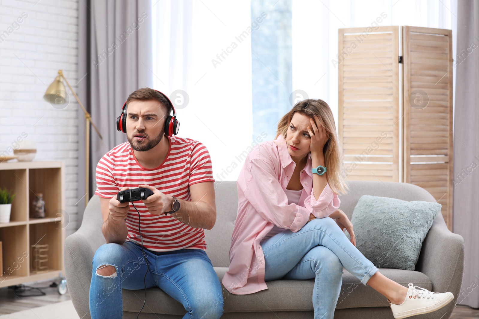 Photo of Young man playing video game at home while his girlfriend angry with him