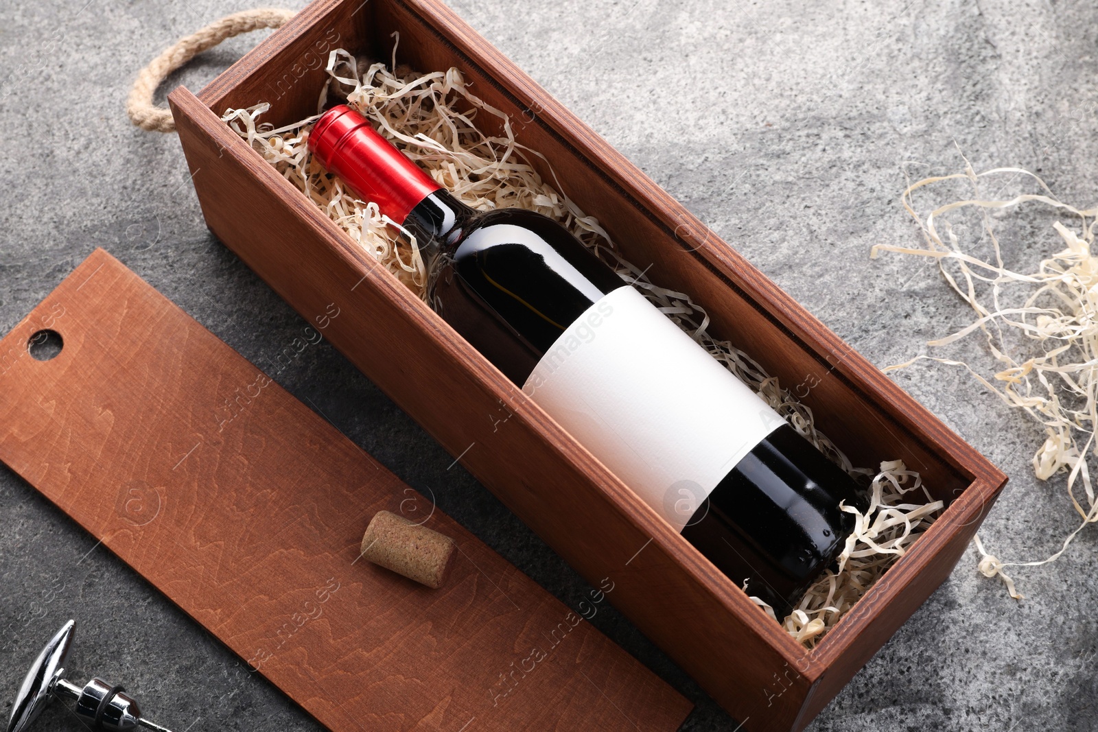 Photo of Bottle of wine in box, cork and corkscrew on dark textured table, above view