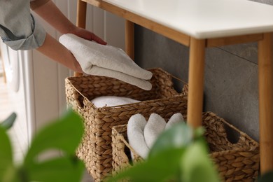 Woman putting towel into storage basket indoors, closeup