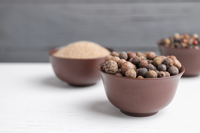 Peppercorns on white wooden table, closeup. Space for text