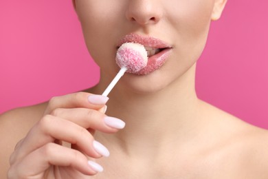 Photo of Young woman with beautiful lips covered in sugar eating lollipop on pink background, closeup