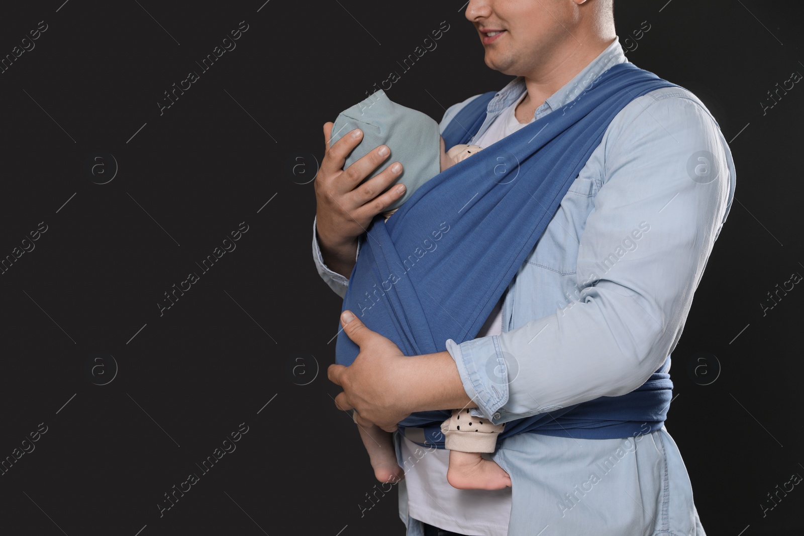 Photo of Father holding his child in sling (baby carrier) on black background, closeup. Space for text