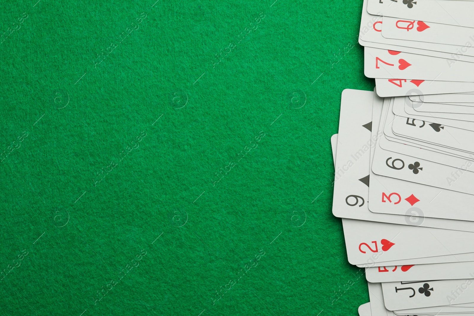 Photo of Deck of playing cards on green table, top view. Space for text