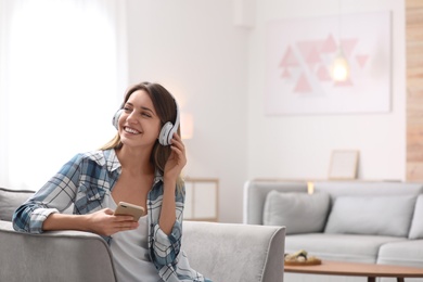 Photo of Young woman with headphones and mobile device resting in armchair at home