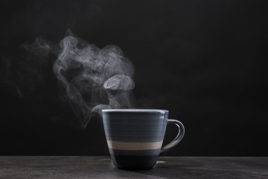 Steaming ceramic cup on grey table against dark background