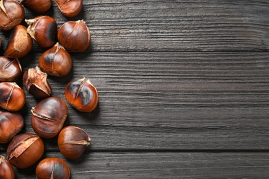 Photo of Delicious roasted edible chestnuts on black wooden table, flat lay. Space for text