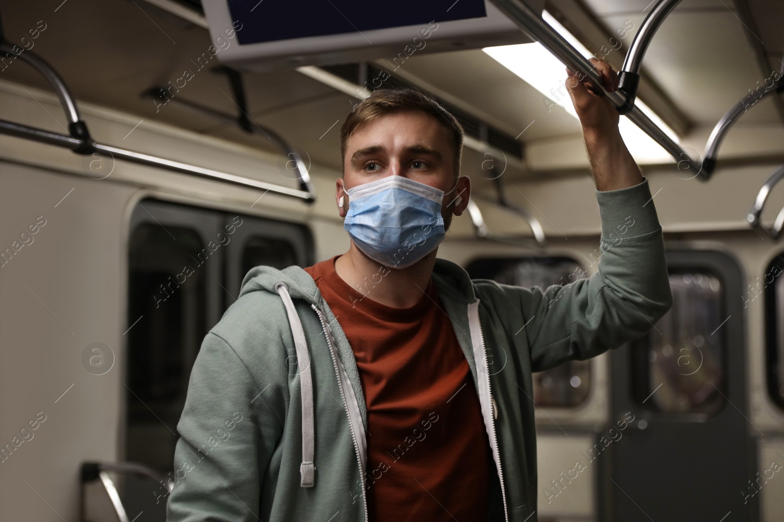 Photo of Young man in protective mask with earphones travelling by subway train. Public transport