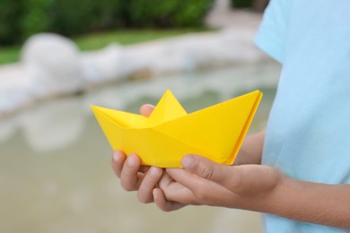 Little girl holding yellow paper boat outdoors, closeup