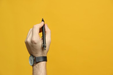 Photo of Left-handed man holding pen on yellow background, closeup. Space for text