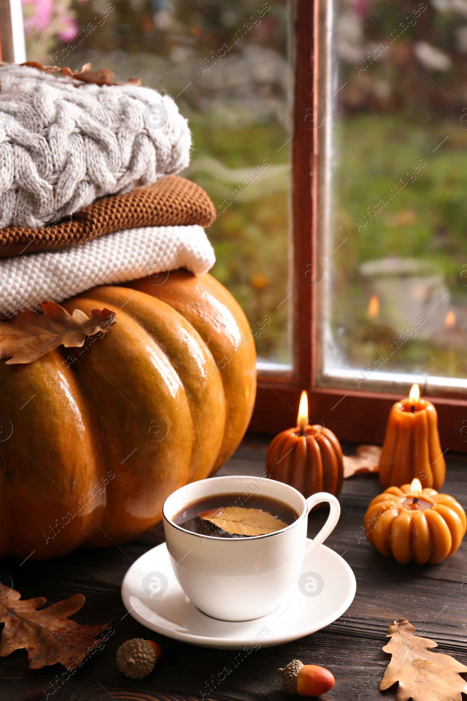Photo of Cup of hot drink and pumpkin shaped candles on wooden table near window. Cozy autumn atmosphere