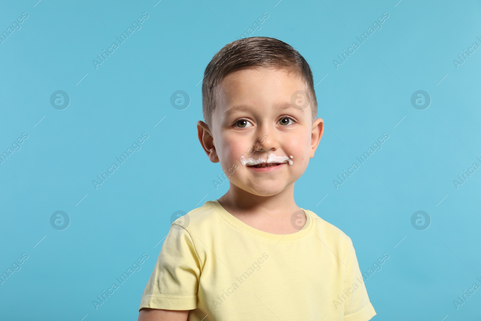 Photo of Cute boy with milk mustache on light blue background