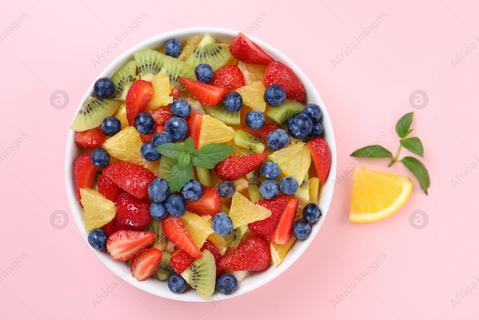 Photo of Yummy fruit salad in bowl on pink background, top view