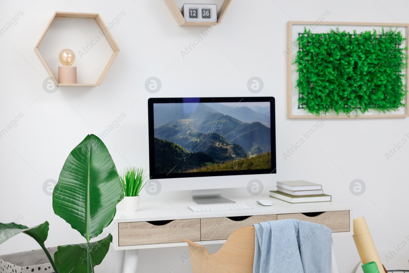 Photo of Green artificial plant wall panel and desk with computer in light room. Interior design